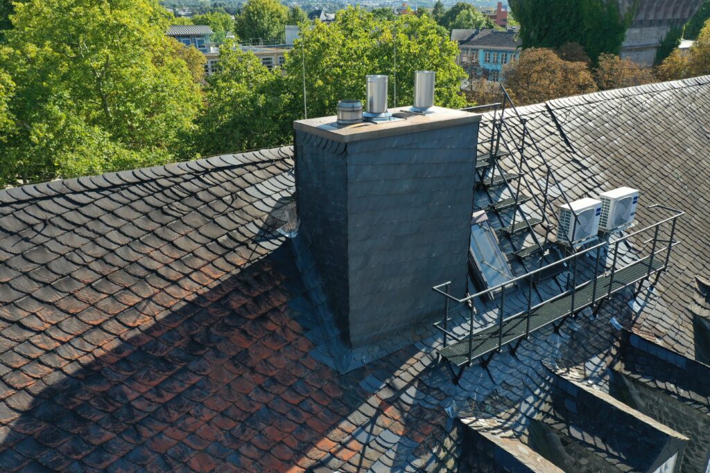 Gesamtansicht der Dachbegehungsanlage mit Klimageräten, Schornstein und Treppenkonstruktion auf einem geneigten Schieferdach.