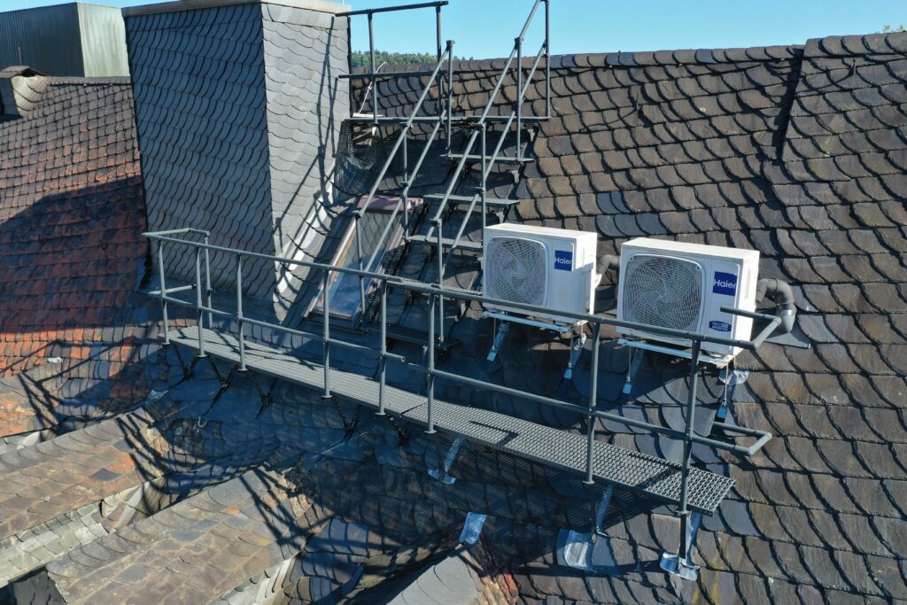 Stabile Dachbegehungsanlage mit Treppe und Geländer sorgt für sicheren Zugang zwischen Dachflächen und Klimageräten.