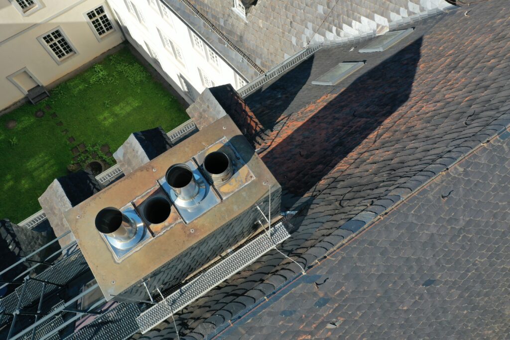 Mehrere Edelstahlkamine ragen aus einem mit Schiefer verkleideten Schornstein, erreichbar über einen gesicherten Dachsteg.
