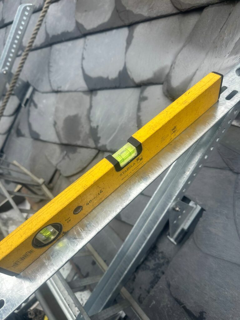 Gelbe Stabila Wasserwaage liegt auf einer Metallschiene auf einem Schieferdach zur Ausrichtung