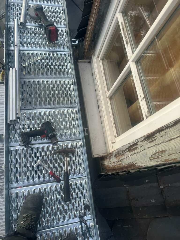 Draufsicht auf Gitterrost mit Werkzeugen wie Hammer, Akkuschrauber und Winkelschleifer neben einem Fenster.