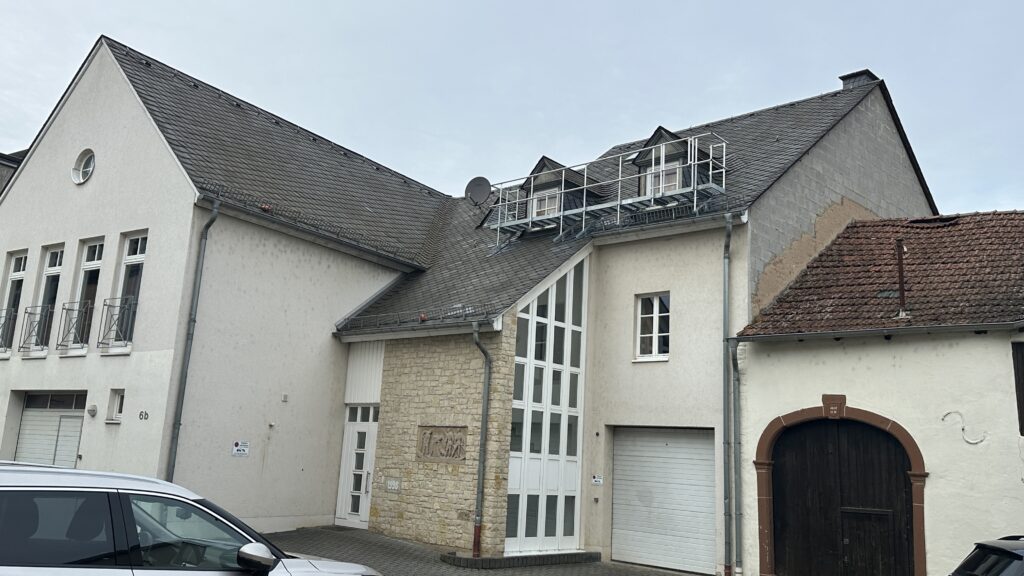 Außenansicht eines Gebäudes mit Schieferdach und neu installiertem metallenen Dachlaufsteg zwischen zwei Gauben.