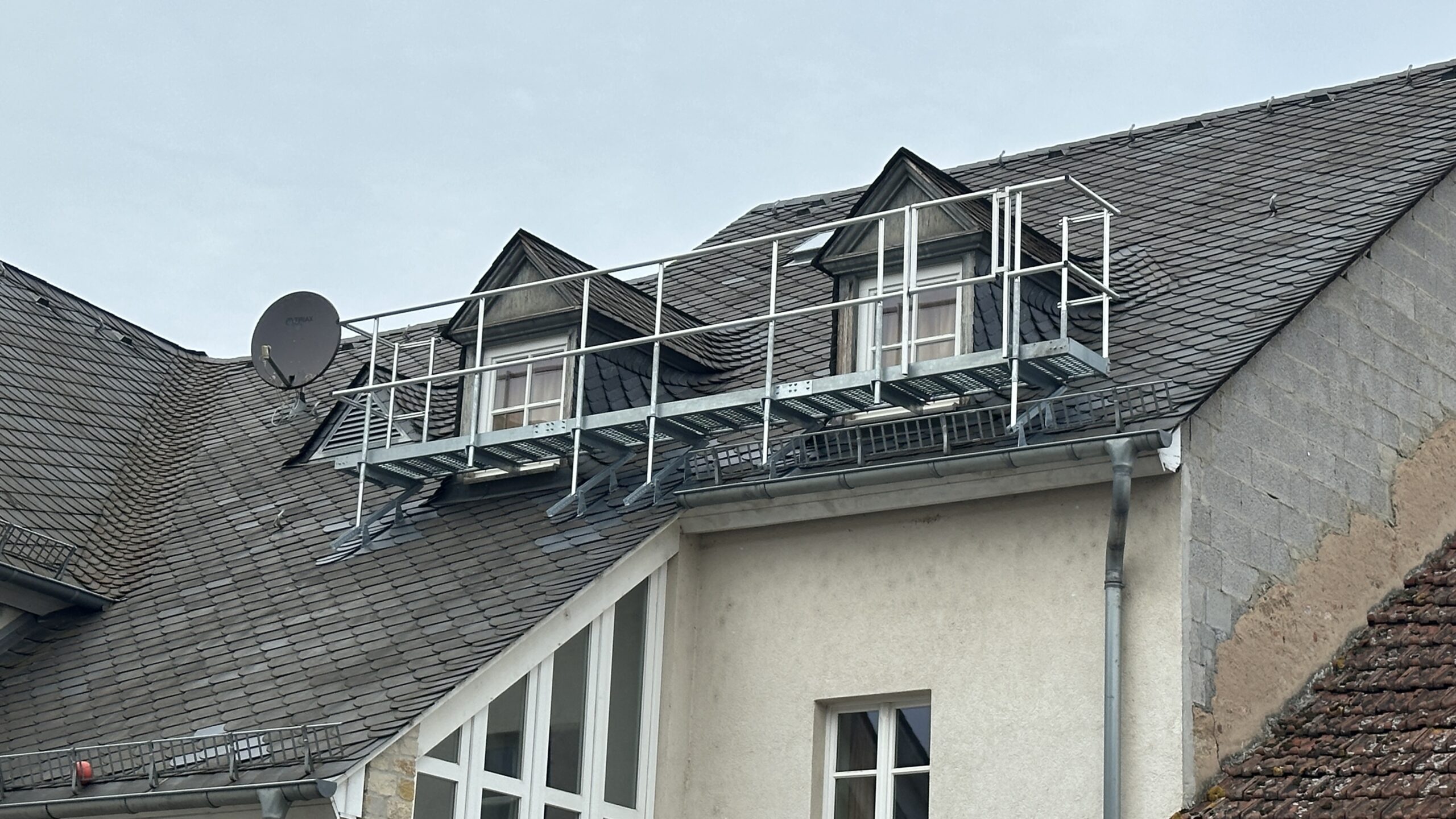 Verzinkter Dachlaufsteg mit Sicherheitsgeländer auf einem Schieferdach montiert.